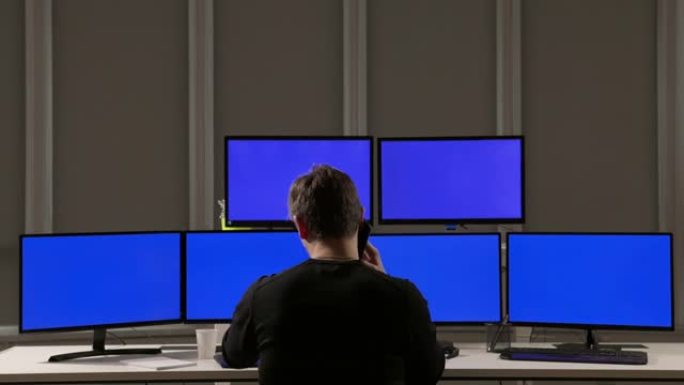 保安在电脑屏幕附近打电话。观察工作场所。