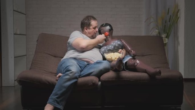 成年男子坐在房间的沙发上看电视，在洋娃娃的陪伴下吃爆米花