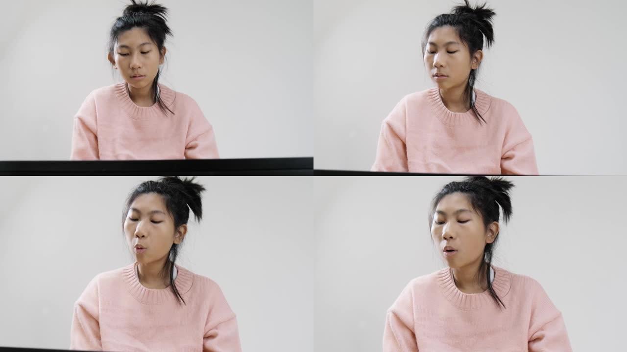 穿着粉红色毛衣的快乐亚洲女孩在灰色背景上学习玩电动键盘，生活方式概念。