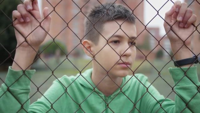 穿着绿色自行车的难民认真男孩独自一人低头在篱笆旁，后悔行动