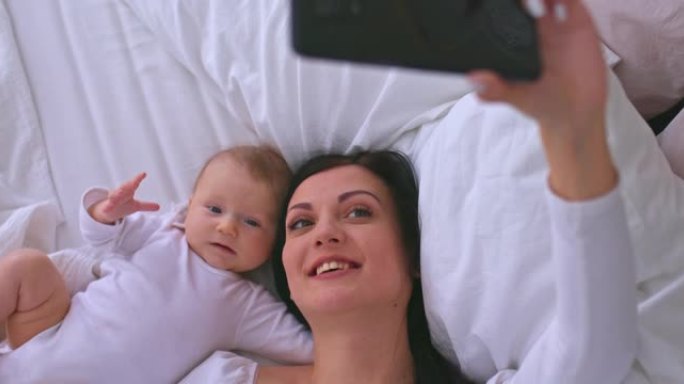 肖像，一个美丽的年轻母亲和一个新生婴儿，在视频链接上与爸爸交谈，妈妈微笑着亲吻婴儿。妈妈在视频通话中