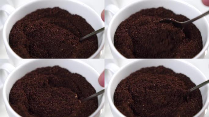 磨碎的未煮熟的咖啡混合在白色杯子中。与茶匙混合