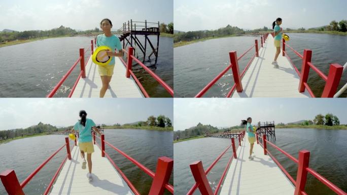 快乐的亚洲女孩在阳光明媚的日子里与家人一起在湖上的桥上奔跑，旅行生活方式的理念。