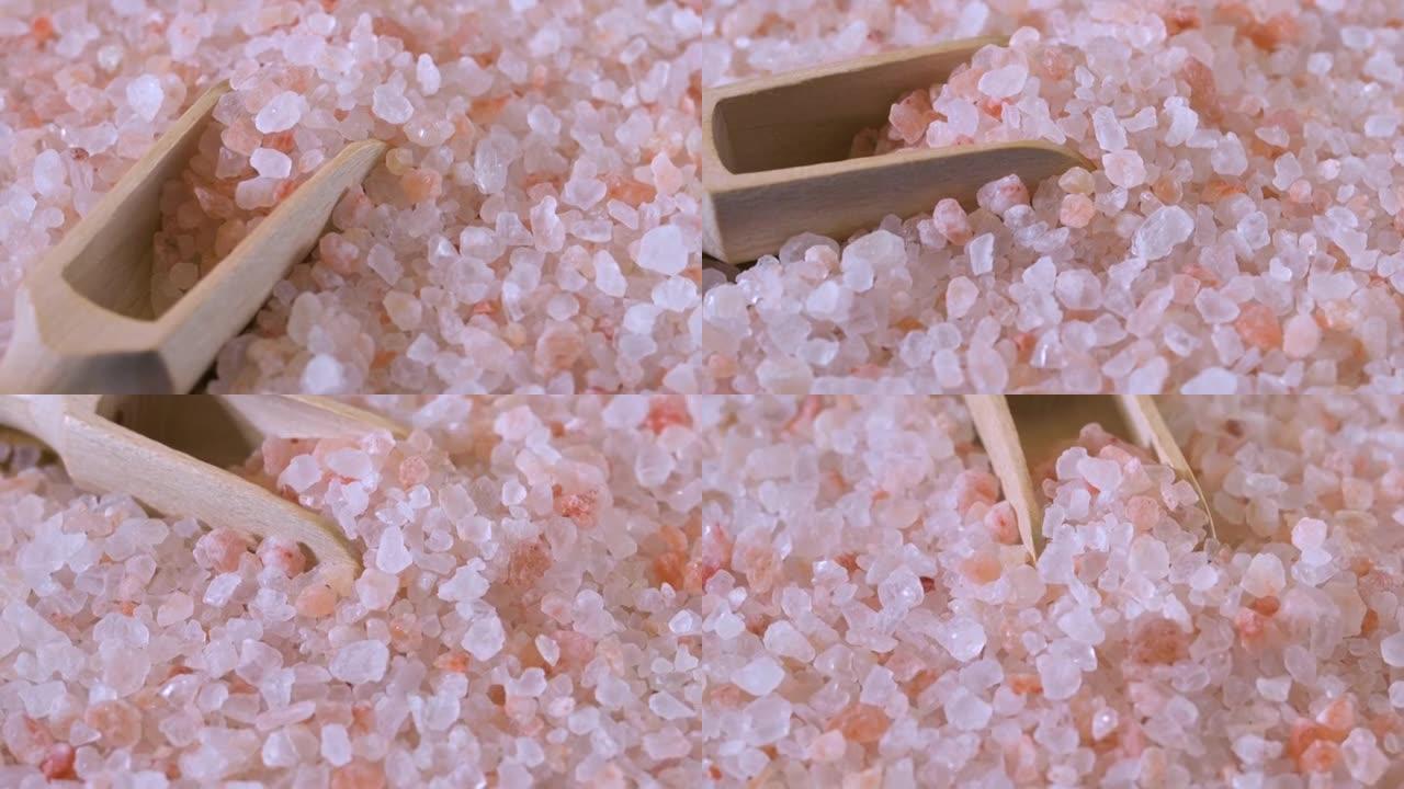 粉色喜马拉雅盐。黑色背景上木勺中的喜玛拉雅粉色岩盐特写。粉色喜马拉雅盐细粒