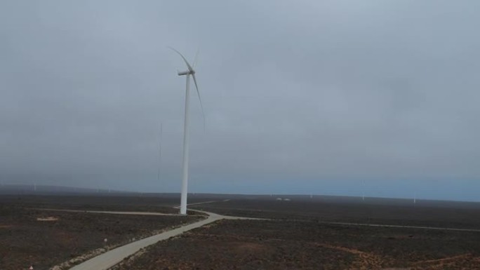 白色风力涡轮机在薄雾中缓慢转动，周围都是棕色的半沙漠景观