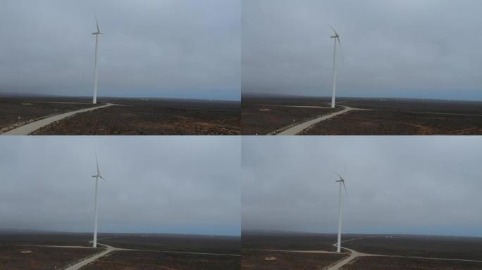 白色风力涡轮机在薄雾中缓慢转动，周围都是棕色的半沙漠景观