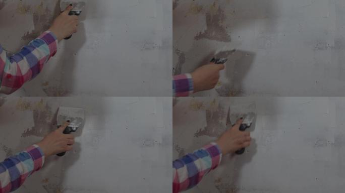 无法识别的人在房间的墙上涂油灰的特写。不知名的女人在公寓里用抹刀抹灰墙。维修工作和改善住房条件的概念