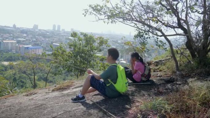 背包客的孩子坐在山顶上，一起看着风景，夏天的生活方式和冒险概念。