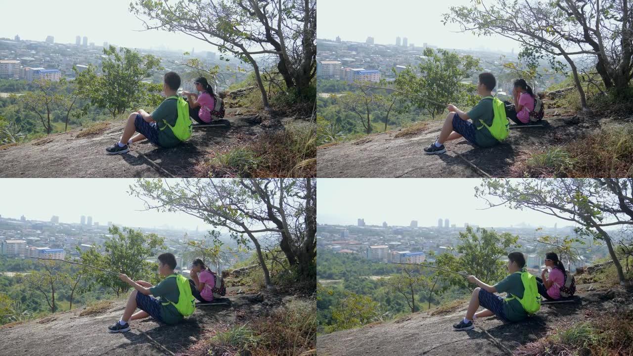 背包客的孩子坐在山顶上，一起看着风景，夏天的生活方式和冒险概念。