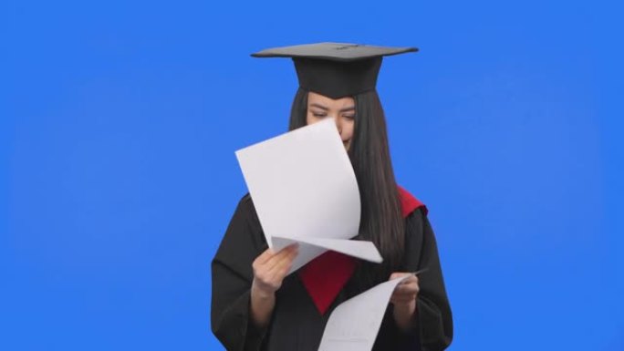 穿着毕业服装的女学生肖像，翻阅文件，撕碎扔掉。年轻女子在蓝屏背景上摆姿势。特写。慢动作准备59.94