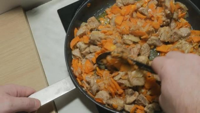 厨师在大锅中煎炸时，将烤猪肉与蔬菜混合。看起来很好吃。洋葱、胡萝卜和香料炒肉。