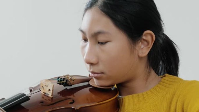 穿着黄色毛衣的亚洲女学生学习小提琴与灰色背景，生活方式概念。
