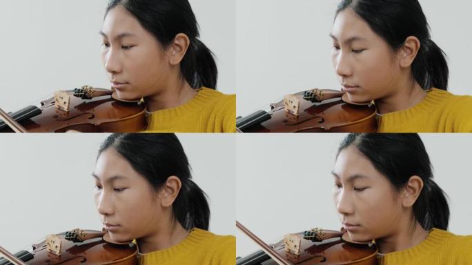 穿着黄色毛衣的亚洲女学生学习小提琴与灰色背景，生活方式概念。