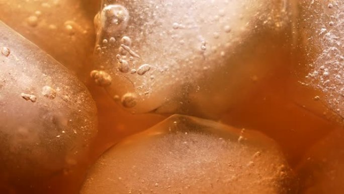金色咖啡饮料中的冰块。气泡漂浮到顶部。早上一种令人振奋、冰冷的夏季饮料。慢动作。特写