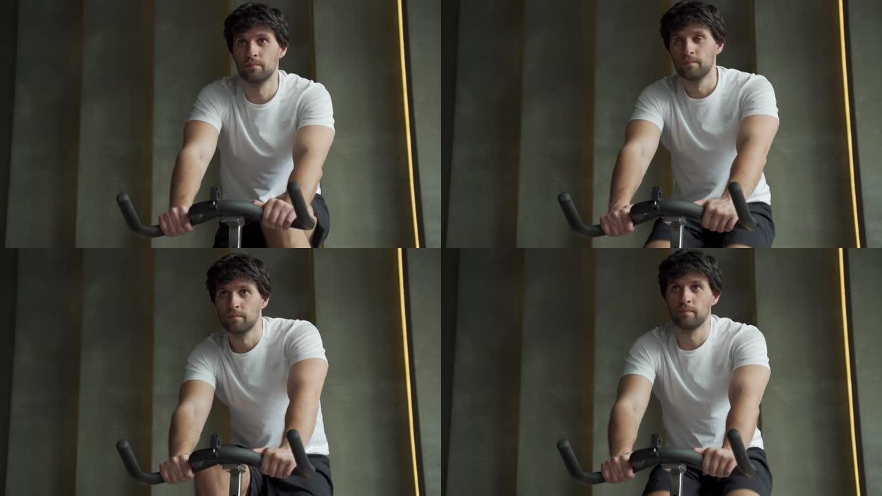 在健身房骑自行车的肌肉发达的人。穿着运动服的运动员骑自行车