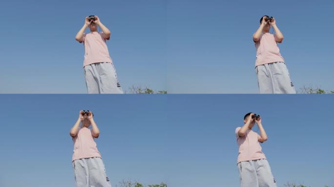 亚洲男孩用双筒望远镜看着山顶上的蓝天，生活方式的概念。
