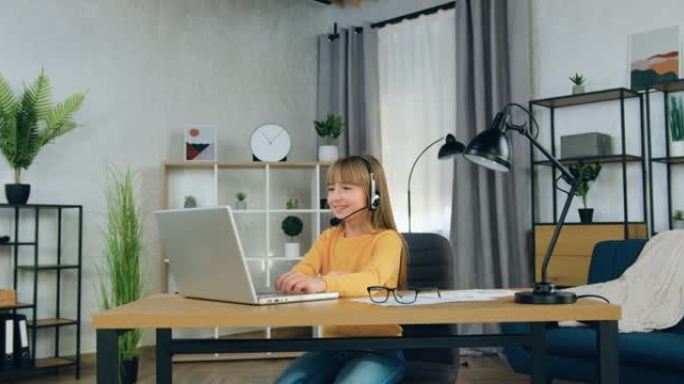 好看的正面自信的初中女孩，戴着耳机坐在笔记本电脑前，在家庭视频会议上与老师交谈，远程学校教育理念