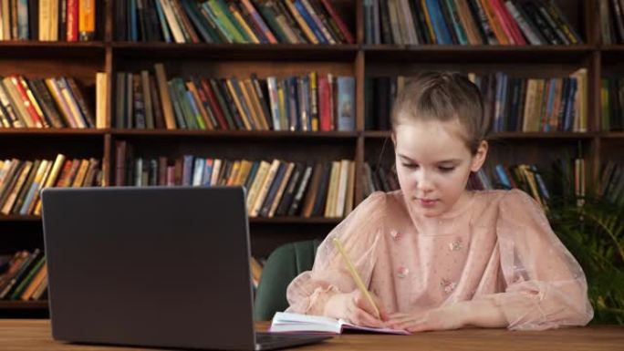 年轻的女士看着笔记本电脑的屏幕并在抄本中写道