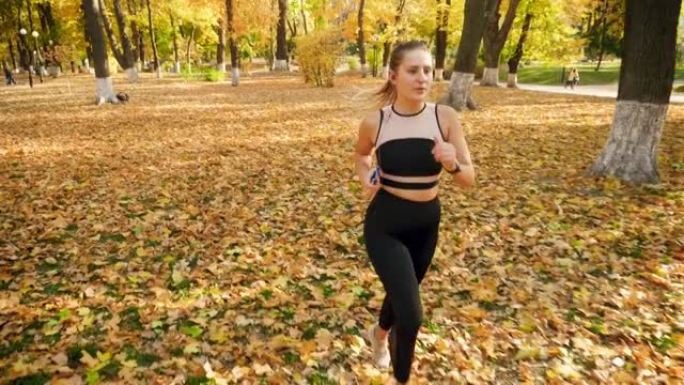 4k慢动作视频来自美女穿着紧身裤的高点，在秋季公园慢跑，用耳机听音乐