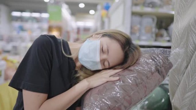 金发长发亚洲女孩，脸上有防护面具，床上用品部门枕头柔软度测试，销售产品，塑料包装，在物流和分销过程中