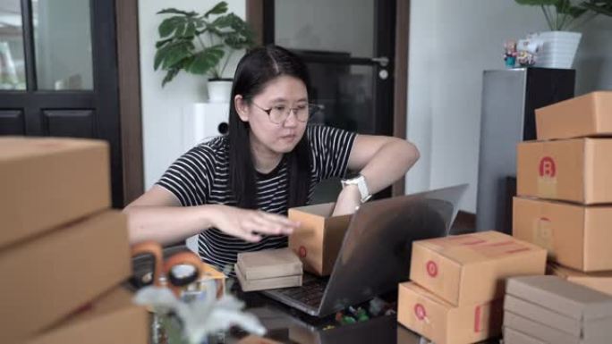 在家庭办公室工作并打包盒子的亚洲妇女准备装运。