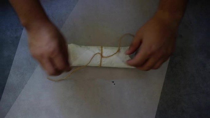 双手解开桌子上滚动的礼物上的绳子制成的线弓