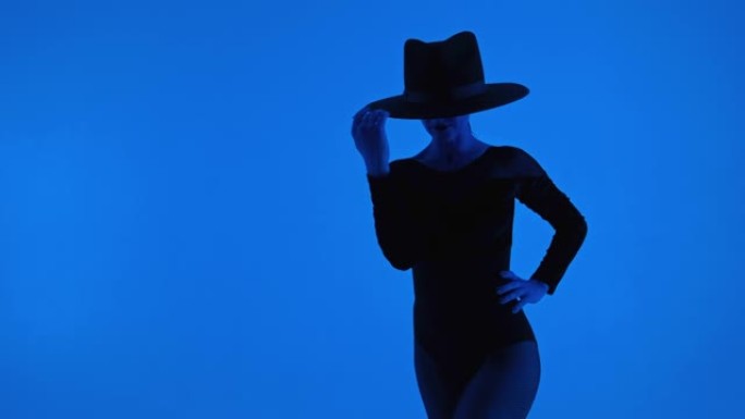 惊人的女士孤立在蓝色背景。戴帽子的专业舞者在摆姿势时表现出当代元素。性感的女人戴着帽子。高质量4k镜