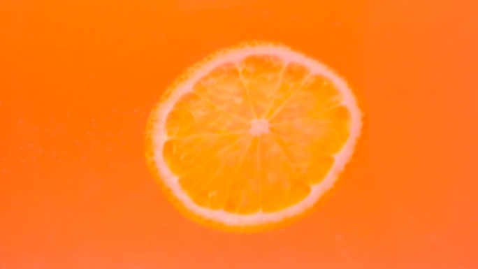 一块橙色落在黄色背景上的水中。水下水果。果汁