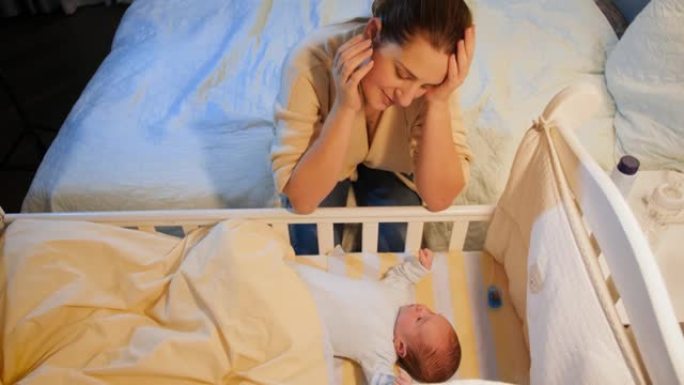 精疲力竭的年轻女子摇着她失眠的新生婴儿的婴儿床。产妇分娩后抑郁和不眠之夜。