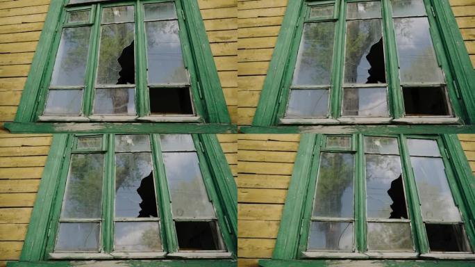 废弃房屋窗户中碎玻璃的玻璃映出了另一棵树和天空。特写拍摄