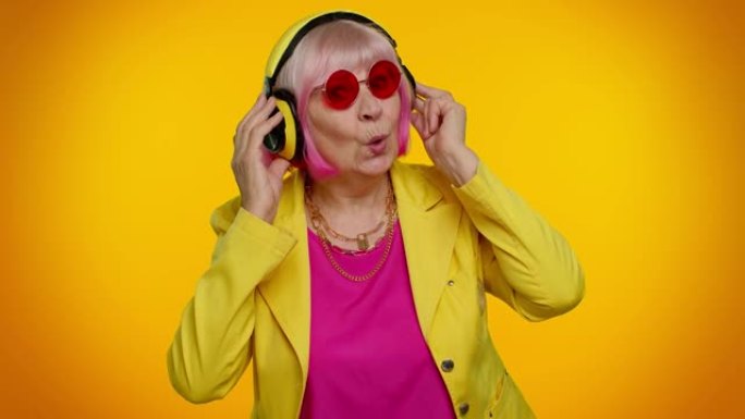 老年妇女戴着耳机听音乐跳舞迪斯科鬼混，玩得开心，比划手
