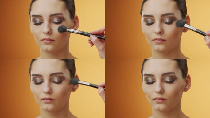 化妆申请的步骤。当化妆师用化妆刷将眼睛下方的区域除尘时，闭上眼睛的女孩脸的特写镜头。