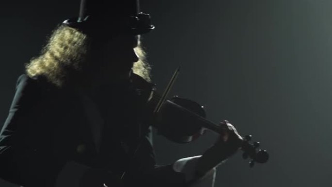 小提琴家音乐家演奏乐器。一个穿着黑色西装和爱尔兰帽子的男人的剪影，用小提琴演奏旋律。带有霓虹灯的黑烟