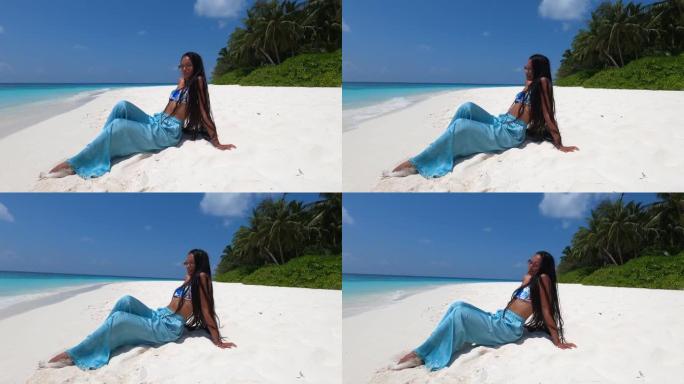 4k视频: 在马尔代夫的暑假期间，坐在沙滩上的亚洲妇女在沙滩上玩乐并享受阳光
