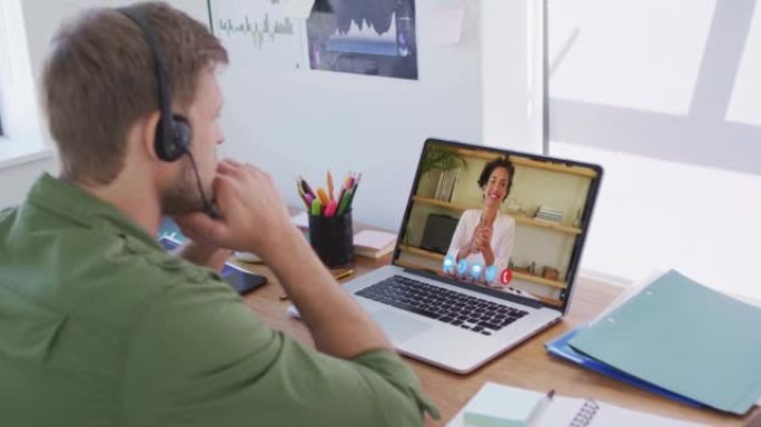 白人男子戴着电话耳机，在办公室的笔记本电脑上与女同事进行视频通话