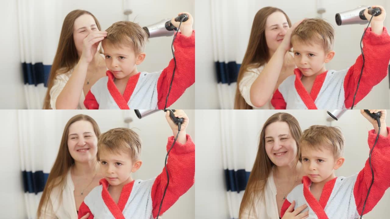 年轻有爱心的母亲在浴室里拥抱和拥抱她的小儿子用吹风机吹干湿头发的肖像。儿童卫生和家庭保健的概念。父母