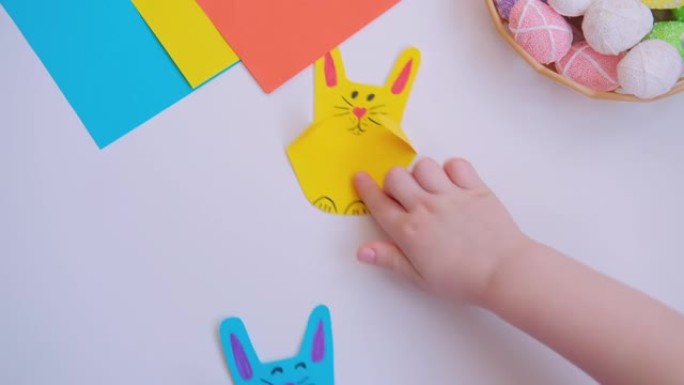 孩子们的手指拿着复活节工艺七彩纸兔子和跳跃。