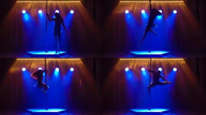 在一个有蓝色霓虹灯的黑暗工作室里，一个运动灵活的女人在一根杆子上旋转。舞蹈飞行元素编舞，健美操，健身