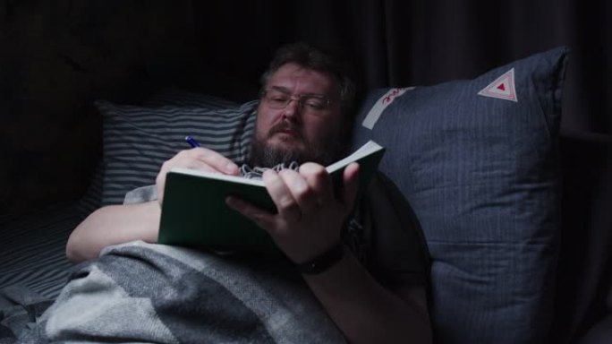 成熟的男人在睡觉前在床上做笔记