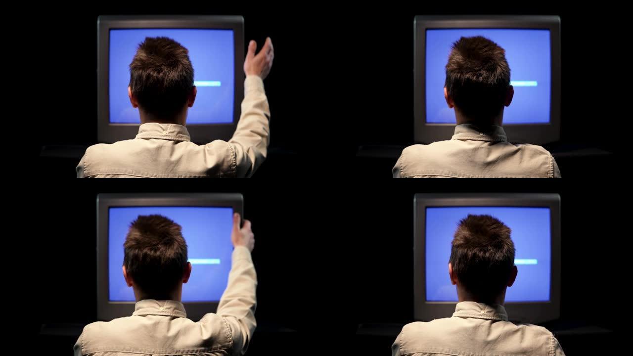 一名男子坐在一台旧电视前的后视图，在黑色背景下的黑暗演播室中，蓝色电视监视器上有噪音干扰。那个人在破