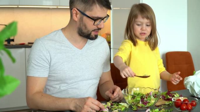 幸福的家庭，父亲和小女儿的乐趣从厨房的蔬菜中准备沙拉。童女喂父亲生菜叶子笑