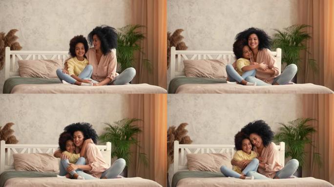 非裔美国妇女和小女孩互相拥抱，聊天很开心。母女俩摆姿势，坐在卧室的床上，内部明亮。慢动作准备，4K，