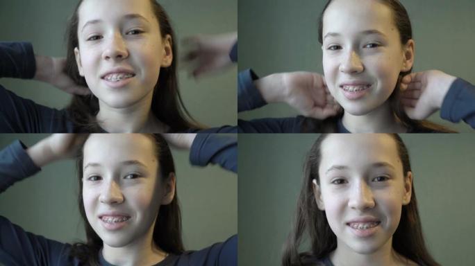 一个戴着牙套的年轻女孩的肖像，看着相机，微笑着拉直她的长发，站在绿色的墙壁上。概念。4k。