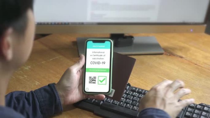 商人使用计算机和智能手机在办公室检查她的COVID-19疫苗接种证书