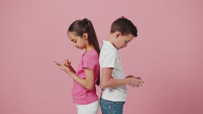 小男孩和女孩背靠背站在智能手机上，好奇的妹妹偷看兄弟手机