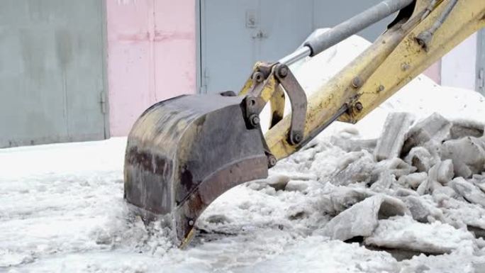 拖拉机铲斗打破了压缩的冰雪。除雪特写。慢动作。