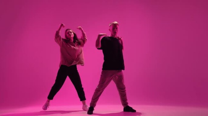 在粉红色工作室灯光下跳舞的年轻夫妇表演。当代富有表现力的激情舞蹈表演