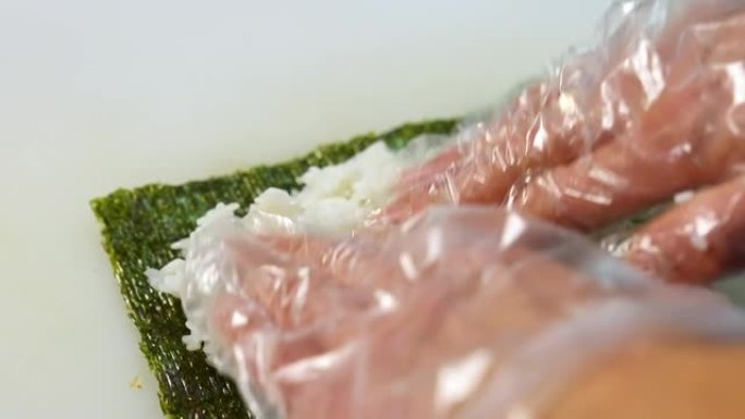 戴着手套的厨师正在烹饪寿司。寿司由米饭、紫菜、黄瓜、奶油奶酪制成。开胃营养食品概念。