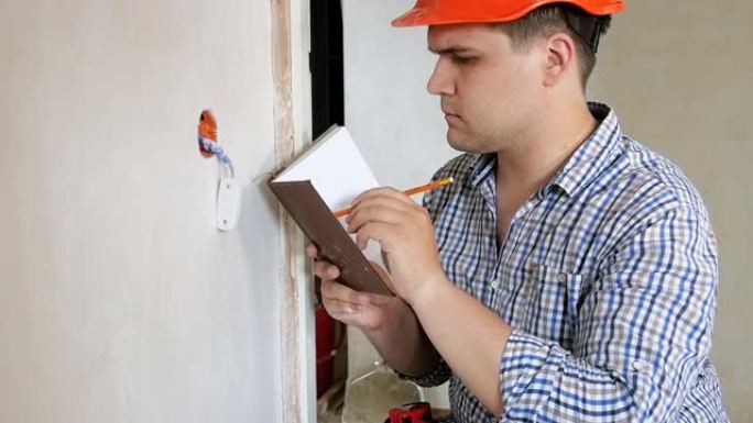 工头在安全帽中的慢动作镜头正在装修中的房屋制作措施并在笔记本上书写