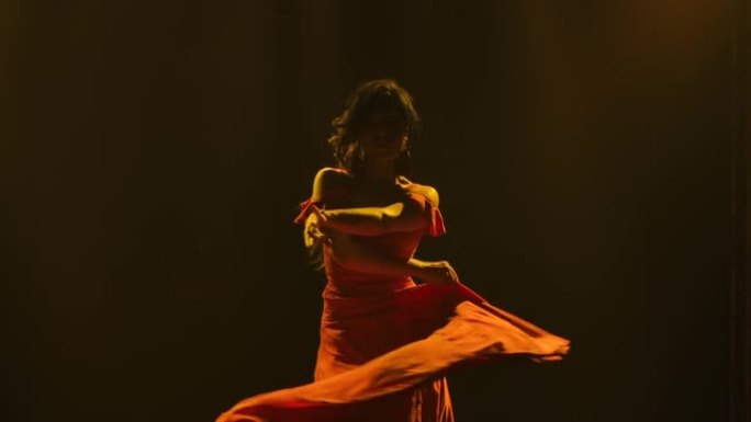 穿着红色长裙的黑发女人在黑暗烟熏工作室的黄色霓虹灯背景下跳舞热情的弗拉门戈舞。特写阿根廷女舞者旋转跳